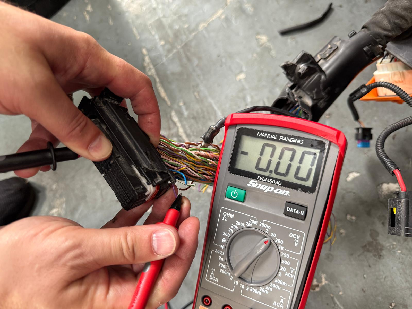 Tehnician electrician auto Carfix din Londra folosind un multimetru pentru a testa pinii unui conector dintr-un cablaj auto complex.