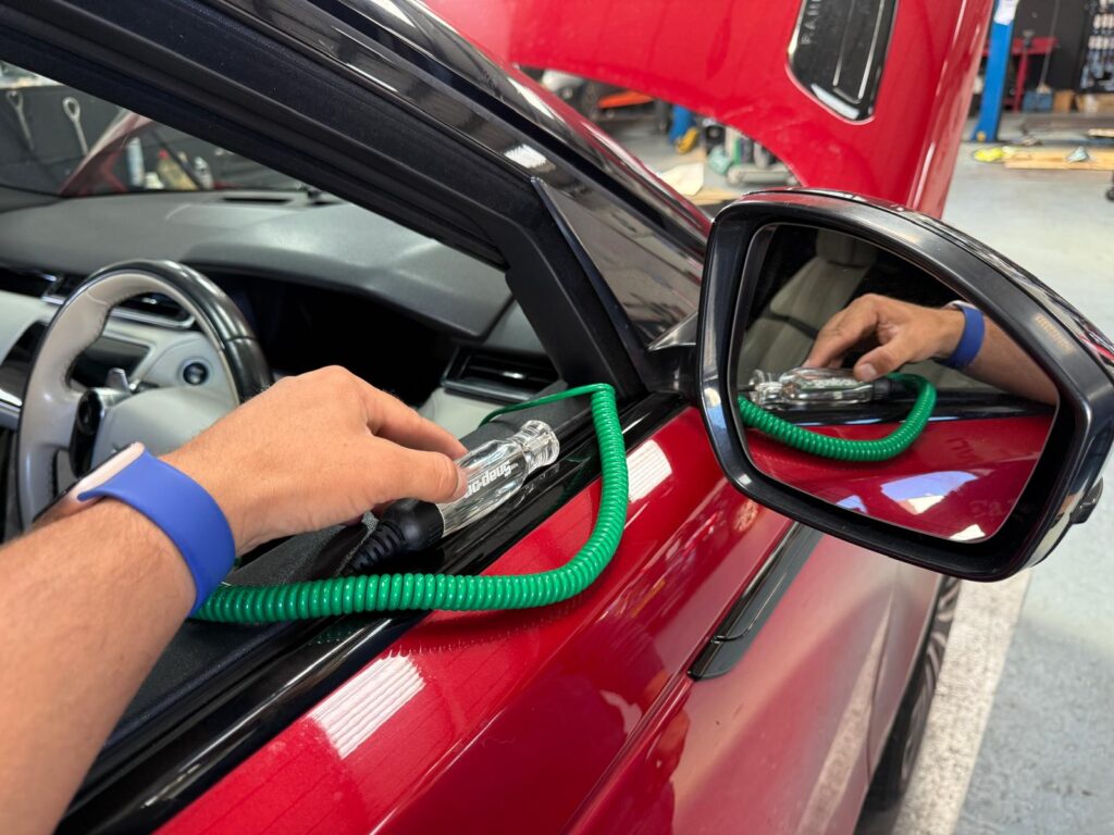 Electrician auto Carfix din Londra folosind un tester de circuit (creion de tensiune) pentru a diagnostica o problemă la geamurile electrice.