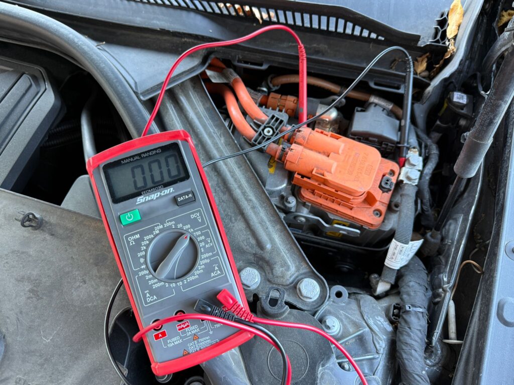 Diagnosticarea unui sistem de înaltă tensiune la un vehicul hibrid, folosind un multimetru profesional conectat la cablurile portocalii.