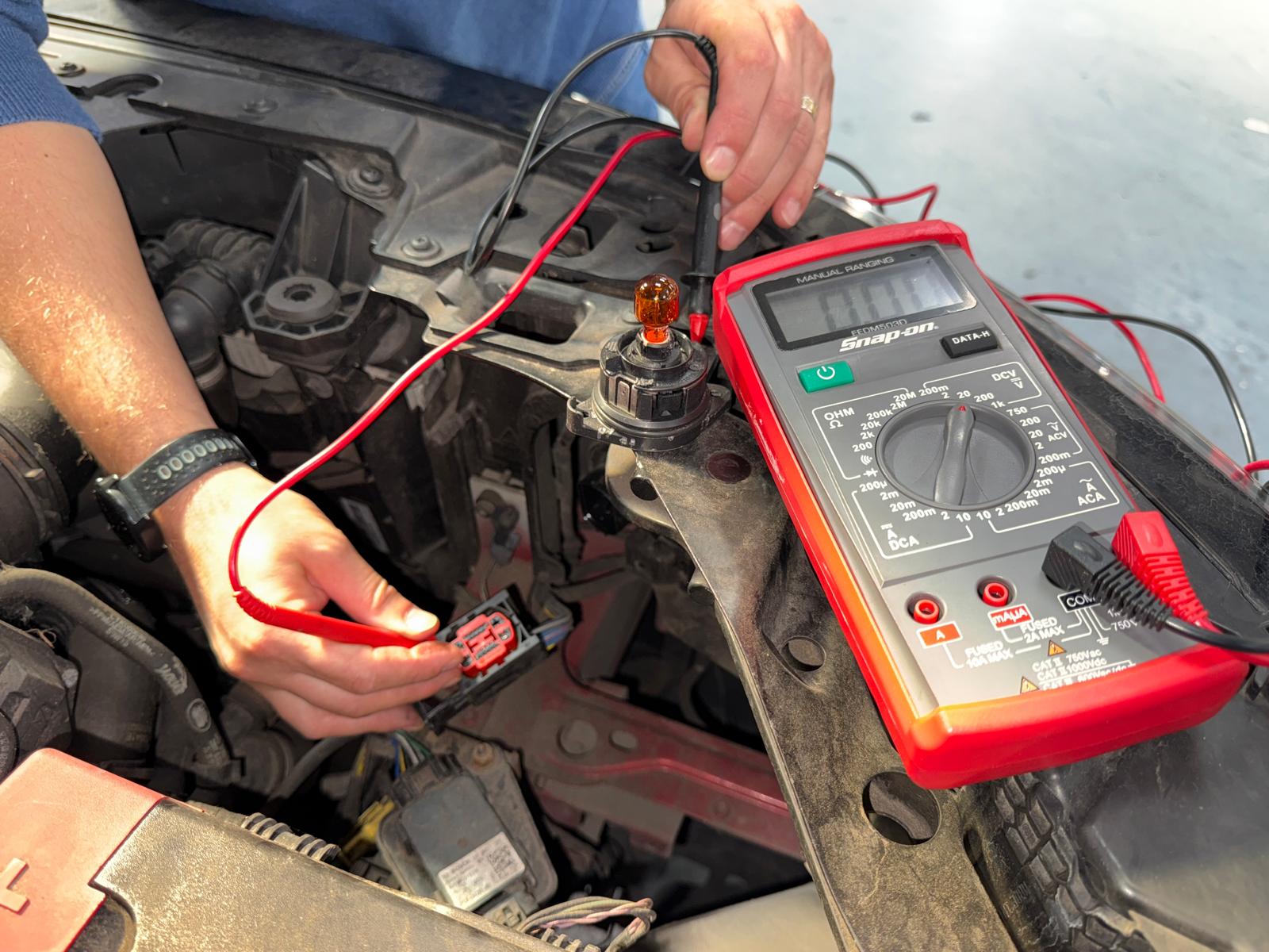Electrician auto Carfix din Londra folosind un multimetru pentru a testa soclul unui bec de semnalizare și a diagnostica o problemă electrică.