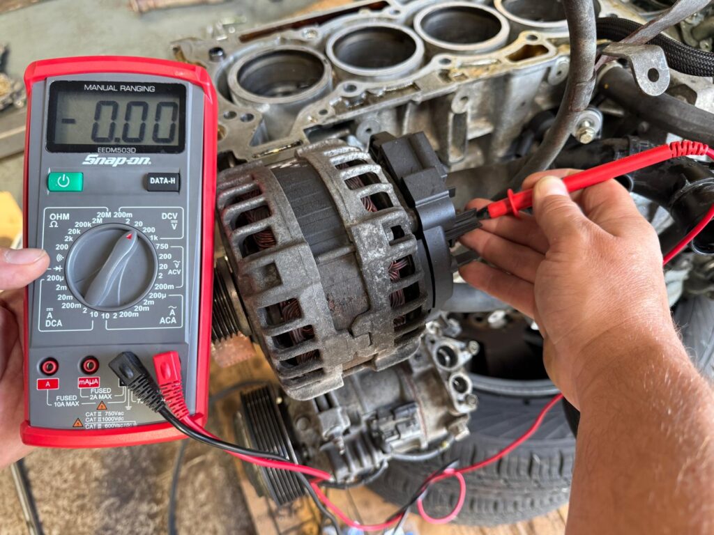 Tehnician electrician auto Carfix din Londra folosind un multimetru pentru a testa pinii unui conector dintr-un cablaj auto complex.