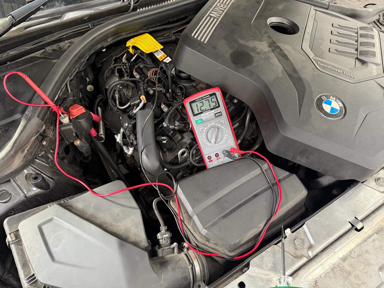 Verificarea sistemului electric al unui motor BMW la Carfix Londra, cu un multimetru ce indică tensiunea corectă a bateriei.