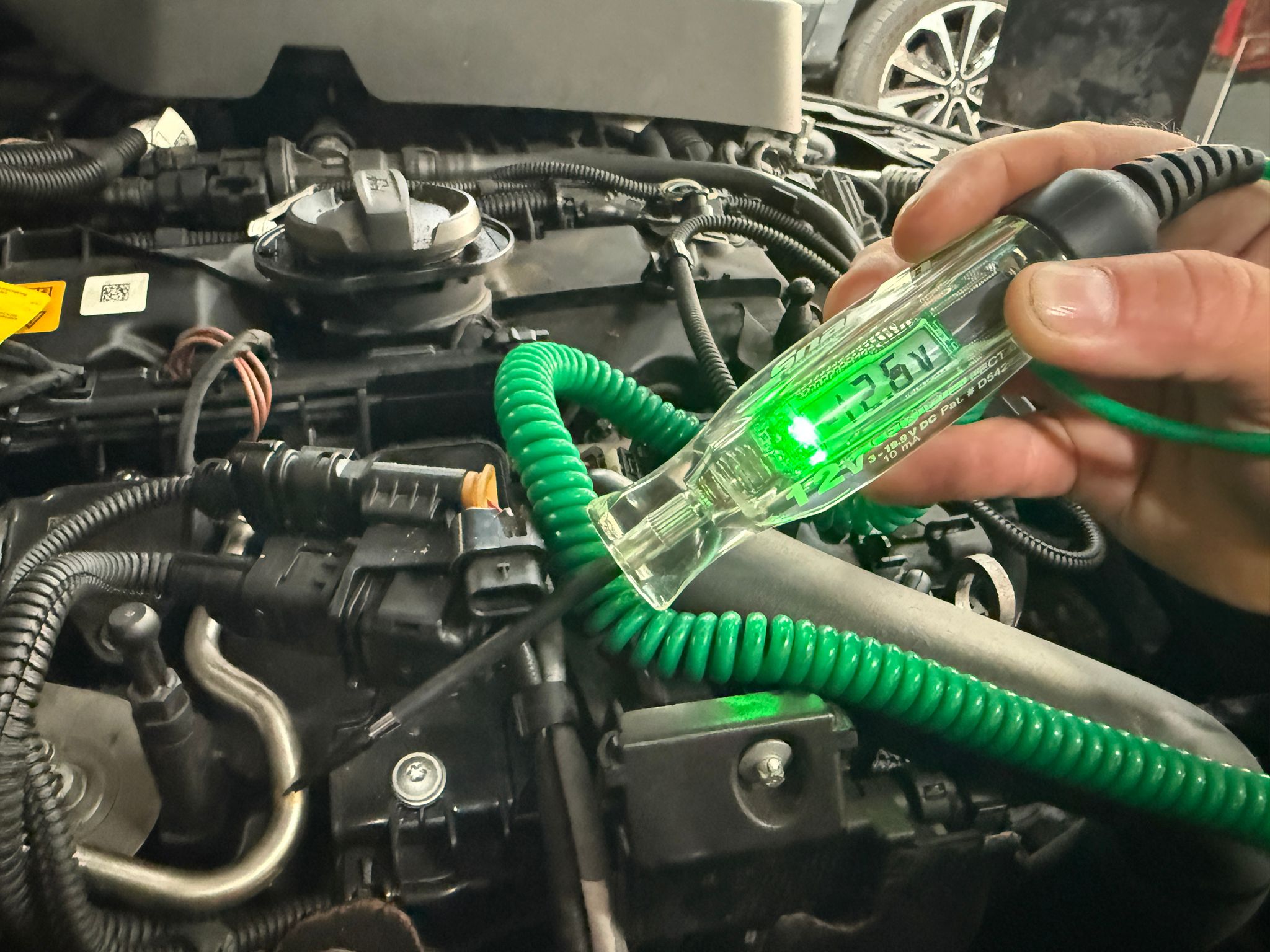 Tehnician Carfix din Londra efectuând o verificare electrică preventivă cu un tester de circuit în compartimentul motor al unui autoturism.