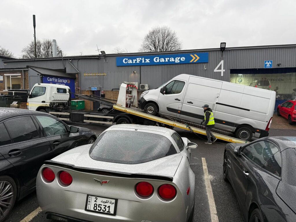O dubă comercială mare, de culoare albă, urcată pe o platformă de tractare în fața service-ului Carfix Garage.