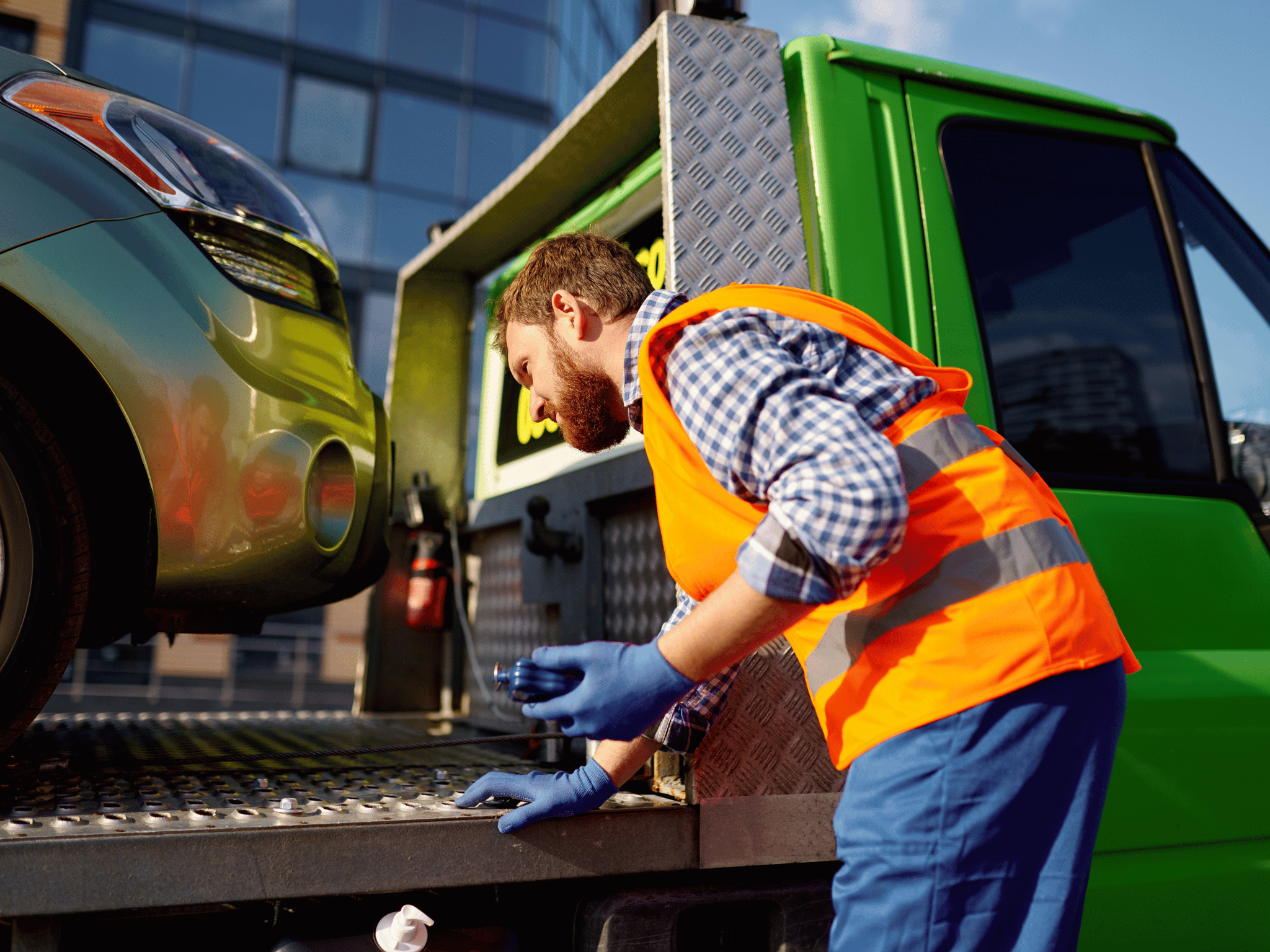 Tehnician în vestă reflectorizantă care fixează un autoturism pe platforma unei autospeciale de tractări auto în Londra.